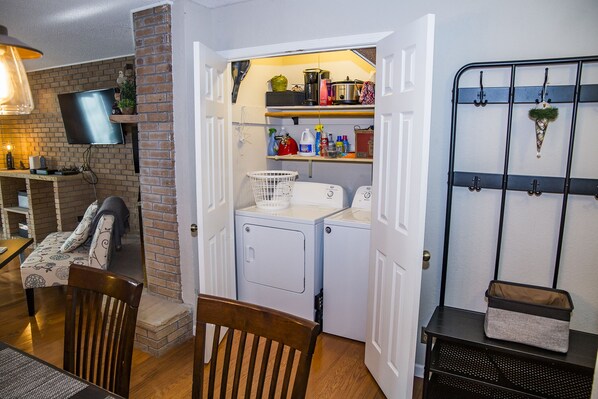 A compact laundry area with a washing machine, dryer, and shelves with cleaning supplies.