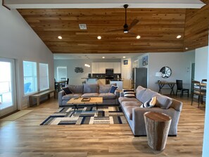 A modern living room with a wooden ceiling, a grey sofa set, a coffee table, and a dining area with a table and chairs.