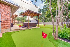 Un patio trasero con césped artificial, zona de barbacoa y una pérgola de madera.