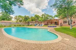 Un patio trasero con piscina, sillas de descanso y una pérgola.