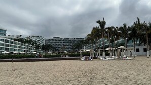 A beach with a row of palm trees and a hotel in the background. - Ocean and swimming front pool view, 6 persons, 2 bedrooms and 2 bathrooms (Bahia De Banderas, Nuevo Vallarta, Bucerias)