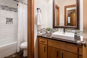 A bathroom with a white bathtub, a white toilet, a wooden vanity with a mirror, and a shower curtain. - Outpost: Nez Perce D6 - Hot Tub Access! (Teton Village)
