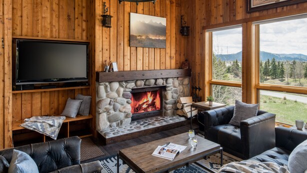 Un salon chaleureux avec une cheminée en pierre, des canapés en cuir, un téléviseur à écran plat et une grande fenêtre donnant sur les montagnes.
