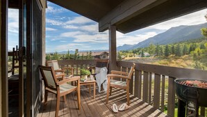 Une terrasse en bois, dotée de chaises et d’un barbecue, qui offre une vue sur un paysage montagneux.