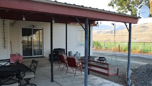 A covered patio with a table and chairs, a swing, and a view of a rural landscape.