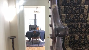 Una escalera con barandilla de madera oscura, alfombra estampada y vista a un comedor con candelabro.