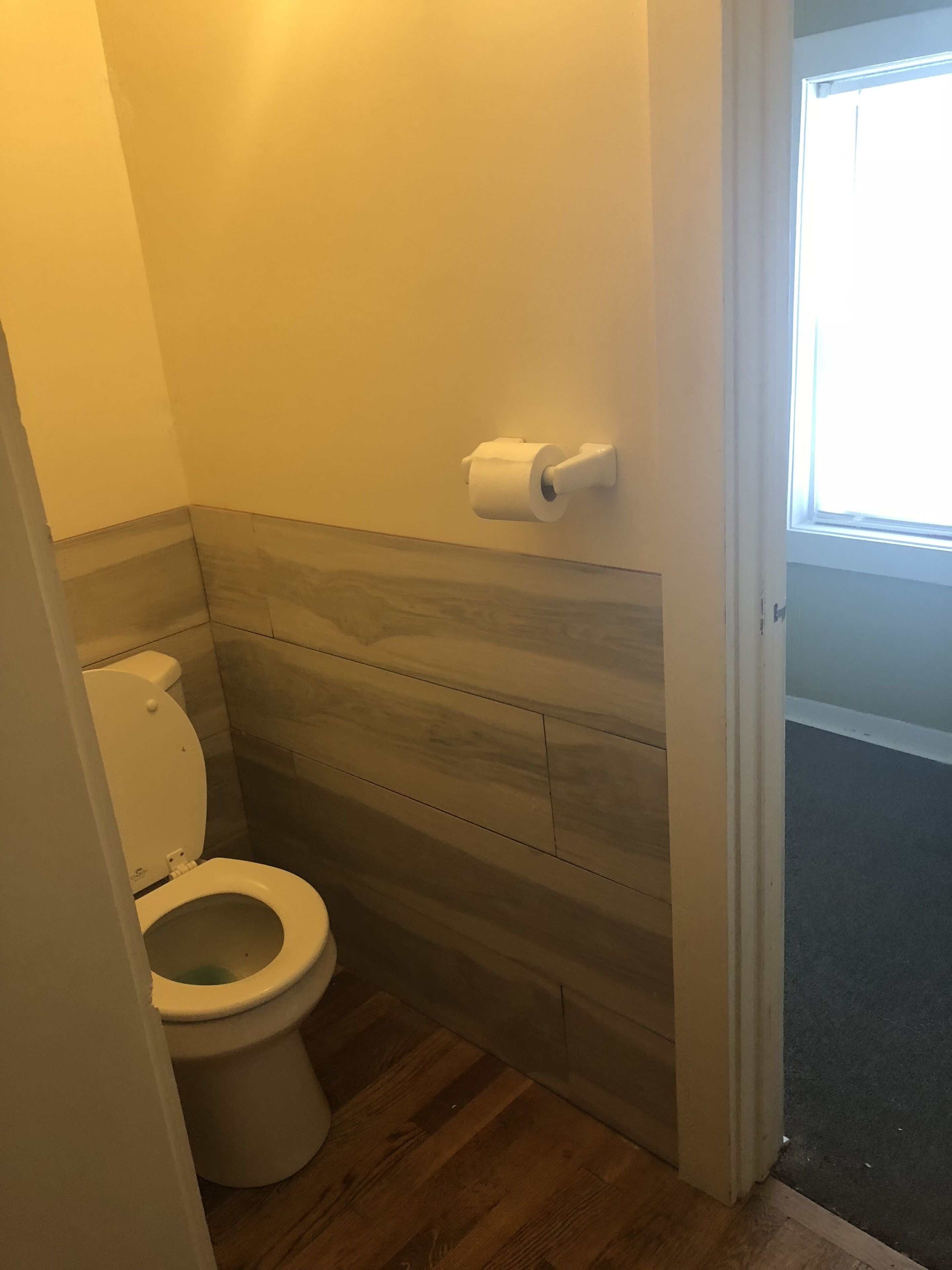 Un baño pequeño con inodoro, paneles de madera y una ventana sobre el inodoro.