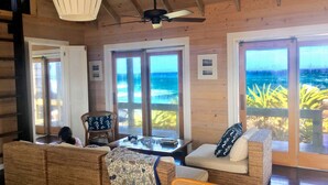 A cozy room with wicker furniture, a ceiling fan, and large windows offering ocean views. - Spectacular Eco Cottage, oceanfront, secret beach (Gregorytown)