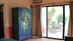 Une pièce avec une grande armoire bleue, une porte-fenêtre coulissante donnant sur un espace extérieur agrémenté de plantes et un sol carrelé.