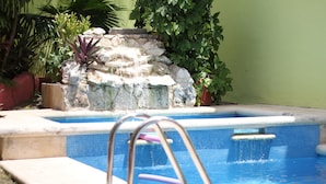 Une piscine agrémentée d’une cascade en pierre, entourée de plantes en pot et d’un mur végétal.