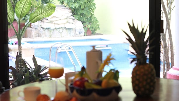 Une table à manger avec un panier de fruits, un ananas et un verre de jus d’orange.