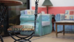 Une chaise avec un coussin à motifs, une table avec un plateau rond et une lampe dans une pièce dont le sol est carrelé, avec un canapé en arrière-plan.