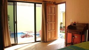Une chambre d’hôtel équipée d’un lit, d’un bureau et d’une porte-fenêtre coulissante donnant sur un espace piscine.