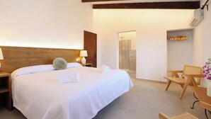 Quarto com uma cama grande, cabeceira de madeira, mesas de cabeceira com luminárias, uma cadeira de madeira e uma pequena mesa.
