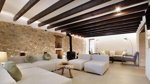 Uma sala de estar aconchegante com parede de pedra, sofás brancos, um banquinho de madeira e lareira.
