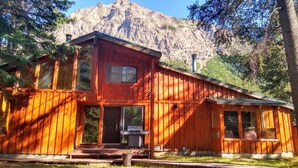 Une cabane en bois dotée d’une grande véranda à l’avant, d’un barbecue et offrant une vue sur une montagne.