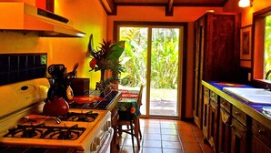 A kitchen with a gas stove, a ceiling fan, and a view of the outdoors through a glass door. -  Enchanting Rainforest Hideaway, on 2 Private Acres to yourself.  Pahoa/Keaau   (Pahoa)