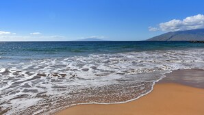 Ein Strand mit Wellen, einem klaren Himmel und einem entfernten Berg.