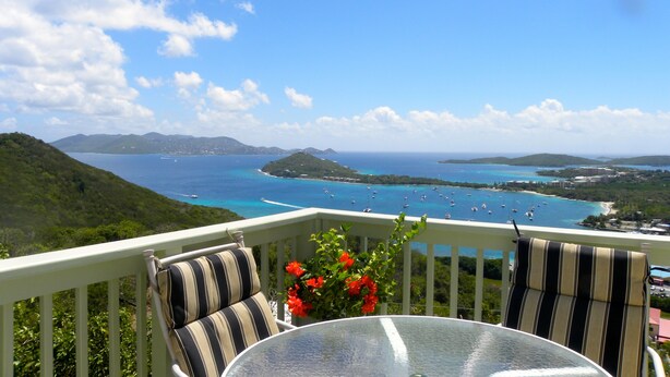A balcony with a glass table and striped cushions, overlooking a coastal view with clear blue waters and distant islands. - Brigadoon: A beautiful Villa In Red Hook sleeps 6 studio is available to rent 2 (St. Thomas)