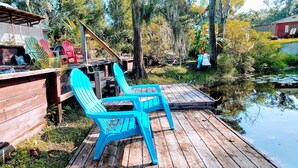 A wooden deck with blue chairs and a small table, surrounded by greenery and a body of water. - 2 kitchens, Canoe, kayak on Sunset Lake + 700sqf apt Perfect for family getaways (Odessa)