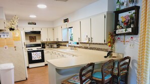 A kitchen with white cabinets, a central island with bar stools, a refrigerator, a stove, and a sink. - 2 kitchens, Canoe, kayak on Sunset Lake + 700sqf apt Perfect for family getaways (Odessa)