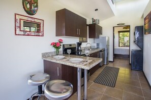 Una cocina compacta con armarios oscuros, una encimera de granito, un taburete pequeño, una cafetera y un refrigerador.