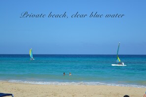 A private beach with clear blue water and two sailboats.