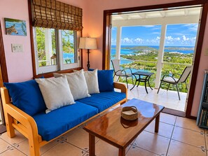 A room with a sofa, a table, and a view of a coastal landscape. - The 'Cottage' at Lion's Gate - Check for our Spring & Summer Specials (Red Hook)