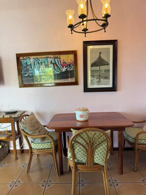 A dining area with a wooden table, wicker chairs, and a chandelier. There are two framed artworks on the wall. - The 'Cottage' at Lion's Gate - Check for our Spring & Summer Specials (Red Hook)