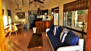A cozy living room with a sofa, coffee table, and dining area. A ceiling fan and chandelier are visible. - The 'Cottage' at Lion's Gate - Check for our Spring & Summer Specials (Red Hook)