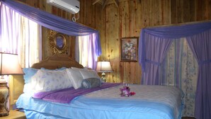 A wooden room with a bed, two bedside lamps, a mirror, and a floral painting. - !Romantic Getaway Or Small Family Fun Time! Hill View Cabins. (Jonesville)