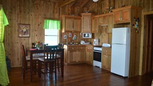 A wooden cabin-style kitchen with wooden cabinets, a dining table with chairs, a refrigerator, a microwave, and a stove. - !Romantic Getaway Or Small Family Fun Time! Hill View Cabins. (Jonesville)