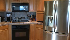 A kitchen with wooden cabinets, a stainless steel refrigerator, a microwave, and a dishwasher. - NEW! Luxury Lakefront Estate with Pool and Putting Greens (Glendale)