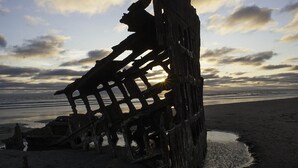 Suuri, rapistunut haaksirikon hyly, joka on ajautunut rannalle, ja taustalla näkyy valtameri.