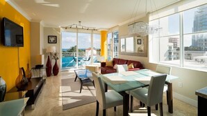 A bright living room with a glass table, a sofa, and a TV mounted on the wall. - Incredible Ocean Views! Luxury 2BD in Heart of South Beach & Steps to the Sand! (Miami Beach)