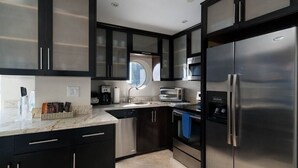 A modern kitchen with dark cabinetry, stainless steel appliances, and a marble countertop. - Incredible Ocean Views! Luxury 2BD in Heart of South Beach & Steps to the Sand! (Miami Beach)