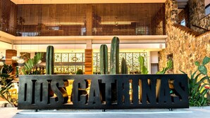 A sign with the text "LOS CARPINTAS" in front of a building with a stone wall and a wooden balcony.