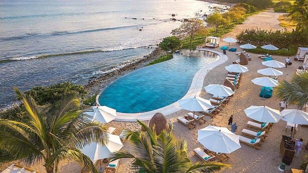 A poolside area with a curved pool, lounge chairs, umbrellas, and a beach view.