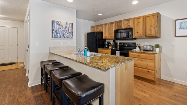 A modern kitchen with wooden cabinets, a granite countertop, and a black refrigerator.