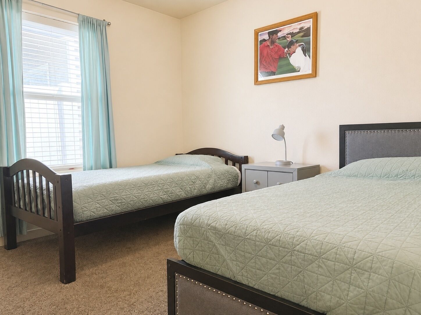 Une chambre avec deux lits simples, une table de chevet avec une lampe, une fenêtre avec des rideaux et un tableau au mur.