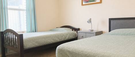Une chambre avec deux lits simples, une table de chevet avec une lampe, une fenêtre avec des rideaux et un tableau au mur.