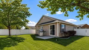 A single-story house with a covered patio, a barbecue grill, and a white fence.