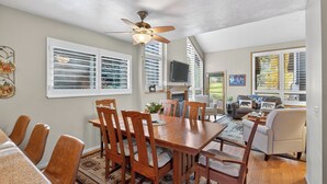 A spacious living room with a wooden dining table and chairs, a ceiling fan, and a fireplace.