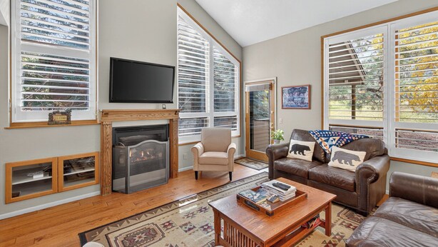 A spacious living room with a fireplace, leather sofas, a television, and large windows with blinds.