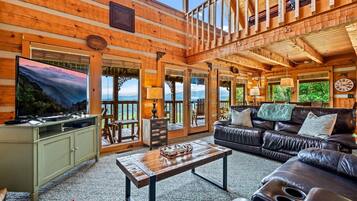 A spacious living room with a large TV, leather sofa, and a wooden ceiling.