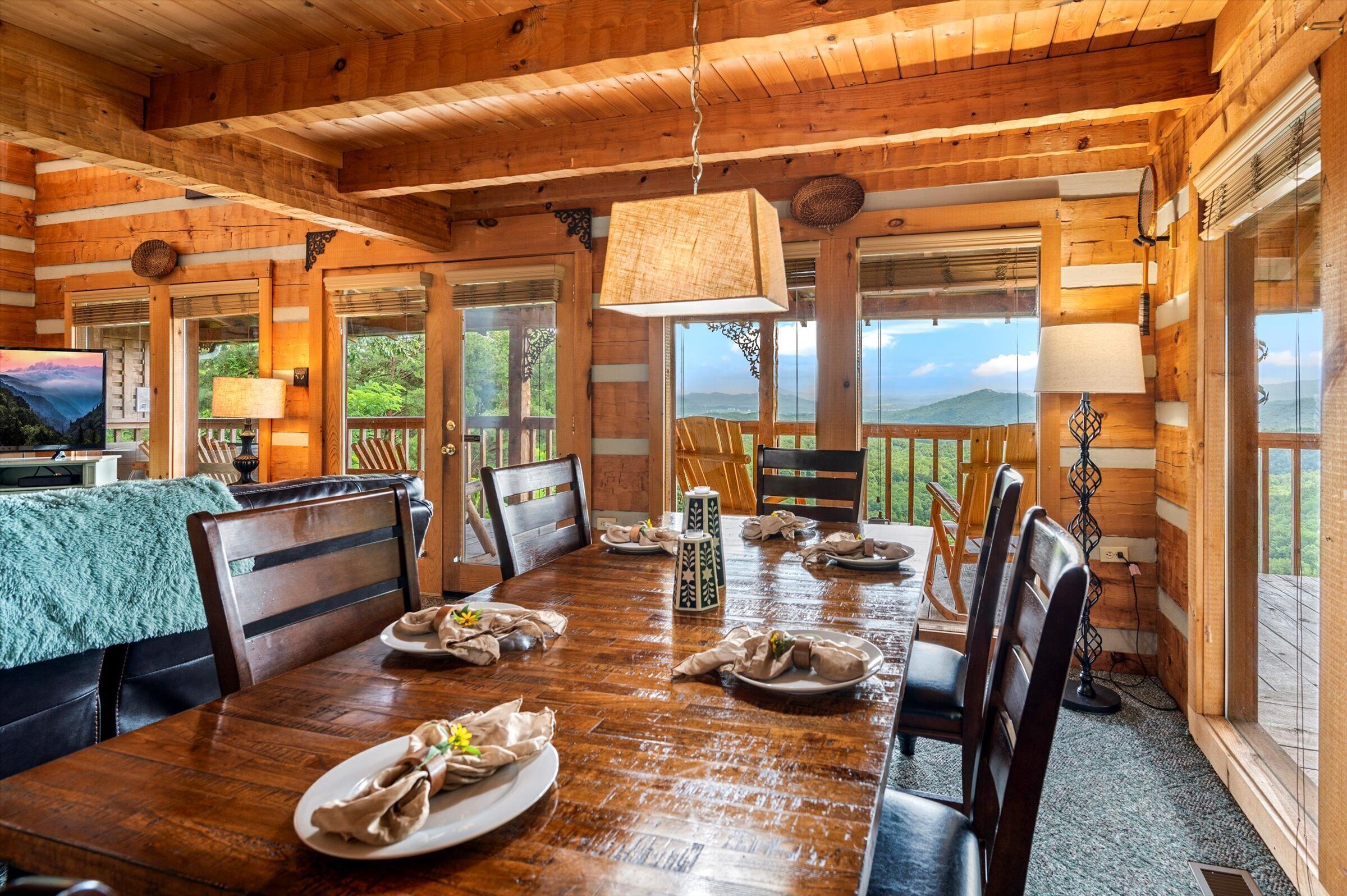 A wooden cabin with a dining table set for four, surrounded by chairs, and large windows offering a view of the outdoors.