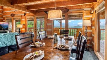 A wooden cabin with a dining table set for four, surrounded by chairs, and large windows offering a view of the outdoors.