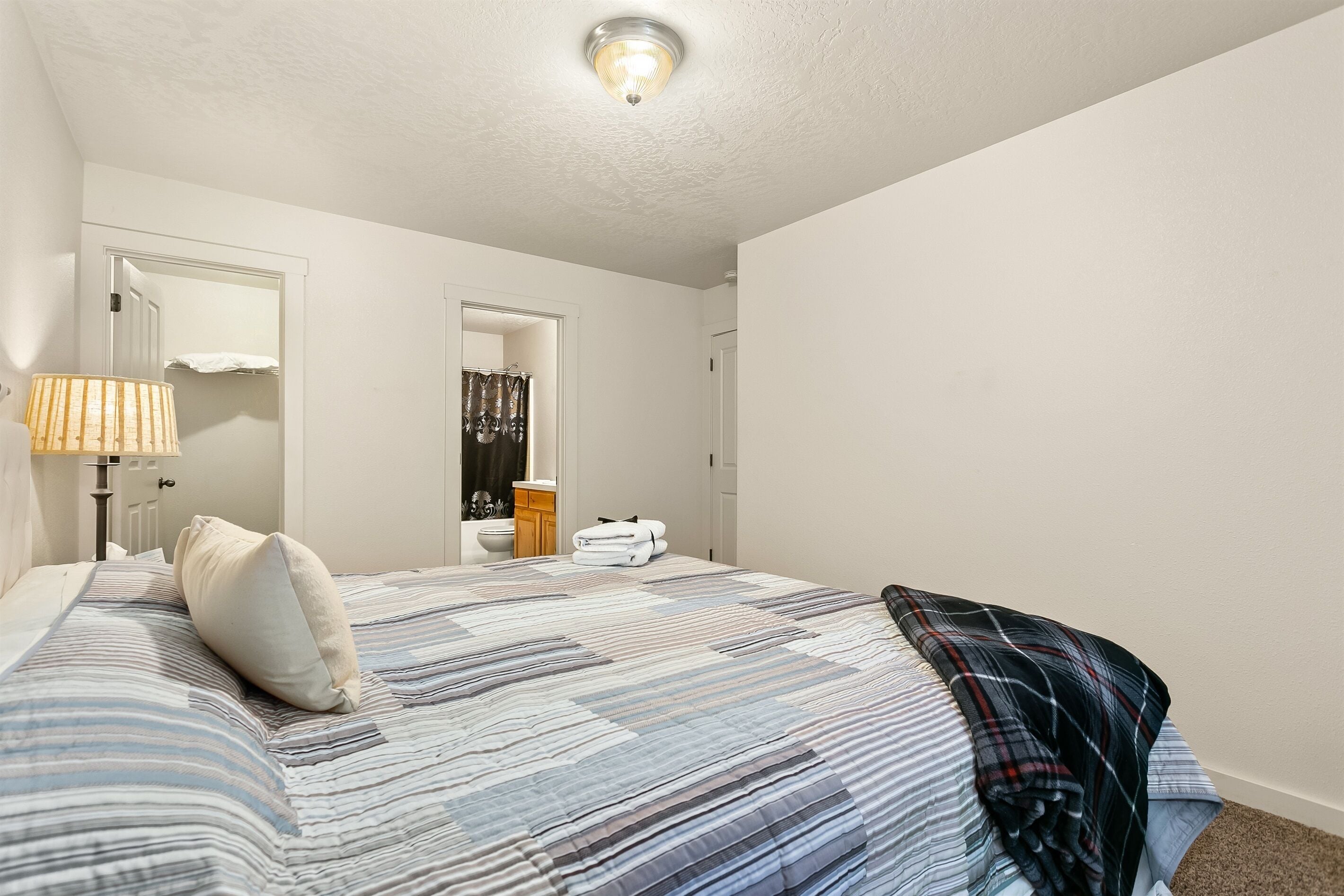 Een slaapkamer met een bed, een bedlamp, een spiegel, een deur en een badkamer die door een open deur zichtbaar is.