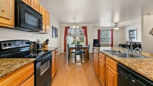 A kitchen with wooden cabinets, a black microwave, granite countertops, a dining table with chairs, a sink, and a dishwasher. - Fenced Yard | Open Concept | Near The Village (Meridian)