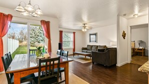 A dining area with a glass table, chairs, and a chandelier. There is a living room with a sofa and a ceiling fan. - Fenced Yard | Open Concept | Near The Village (Meridian)